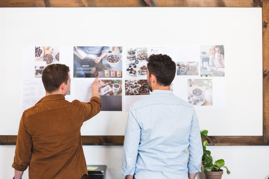 Two male designers stood at a whiteboard reviewing prints of chocolate photography