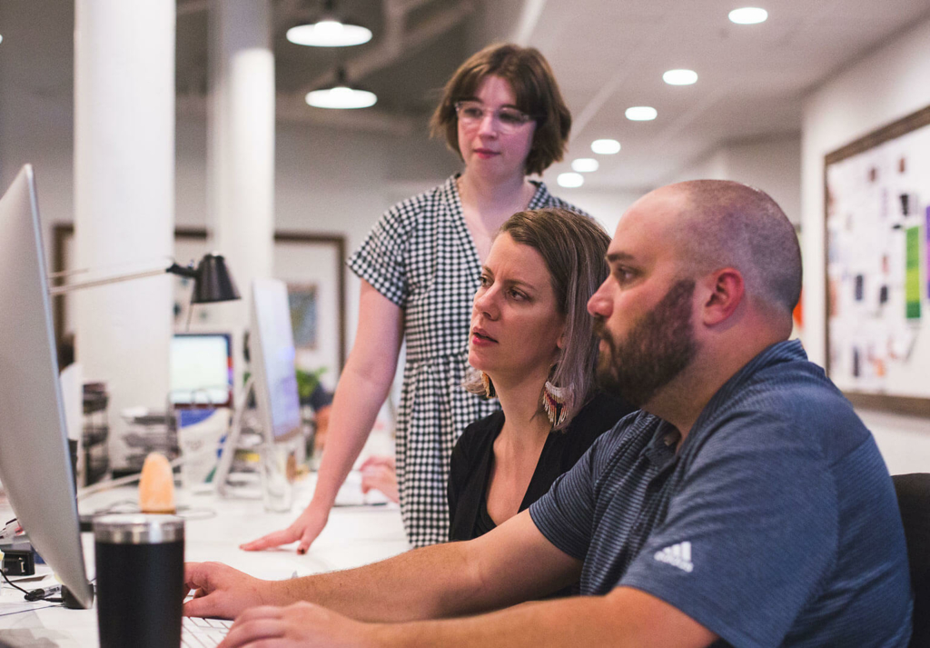 Team member, Ryan, sat working at computer next to two female team members.